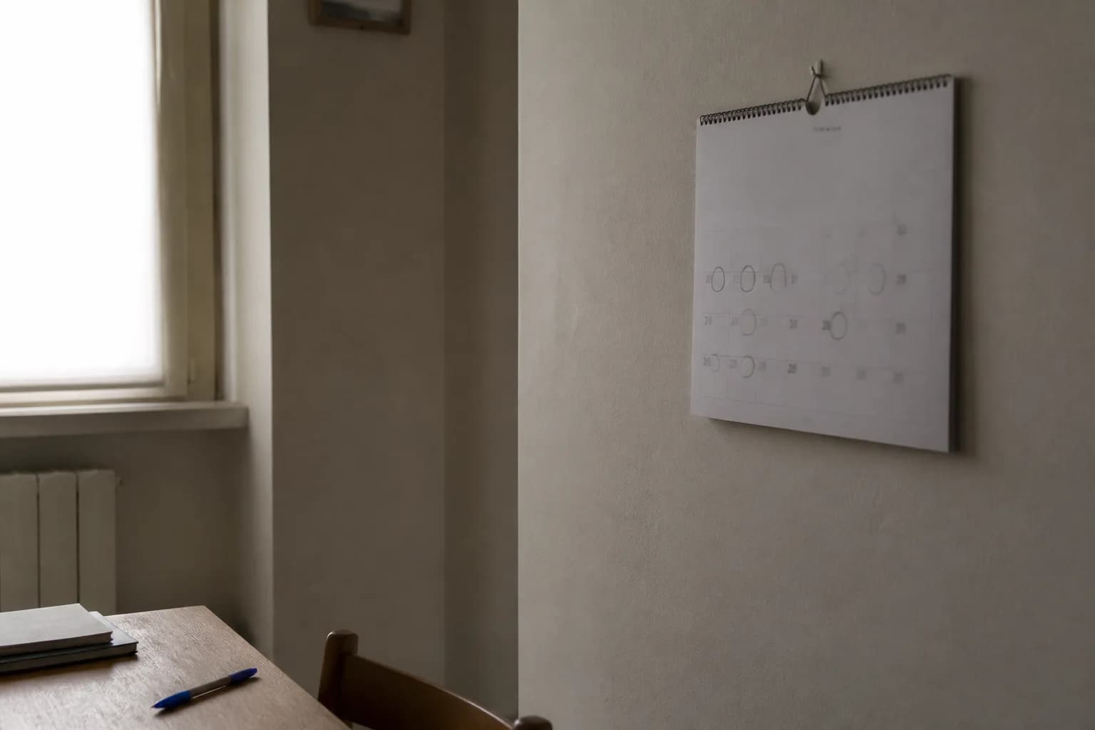 Calendario cartaceo a muro con alcuni giorni cerchiati a penna, ogni cifra totalmente fuori fuoco e illeggibile.