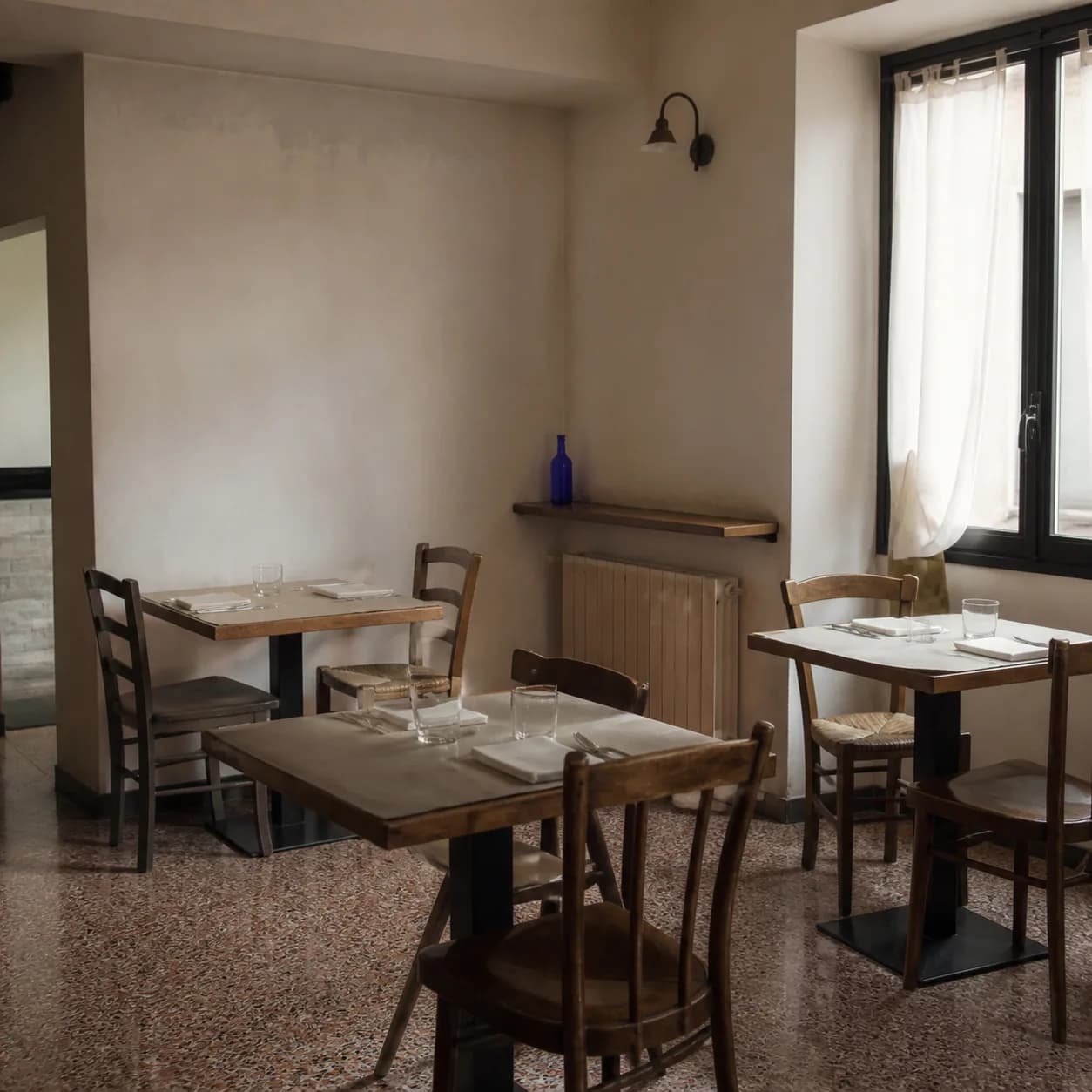 Sala vuota di un ristorante italiano con tavoli apparecchiati in modo semplice nella luce naturale del mattino.