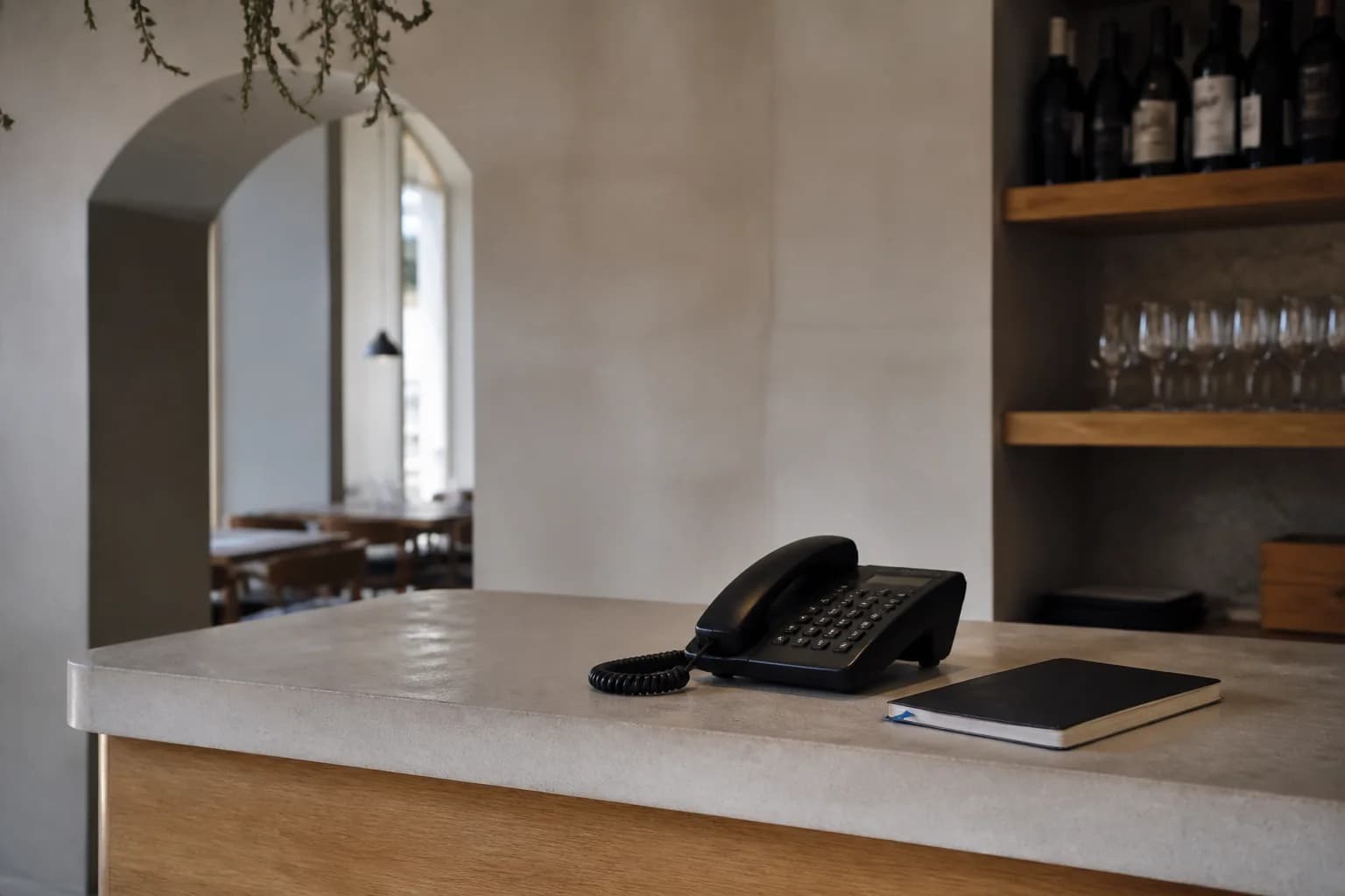 Telefono su bancone reception di un ristorante con taccuino delle prenotazioni chiuso accanto, nessun testo.